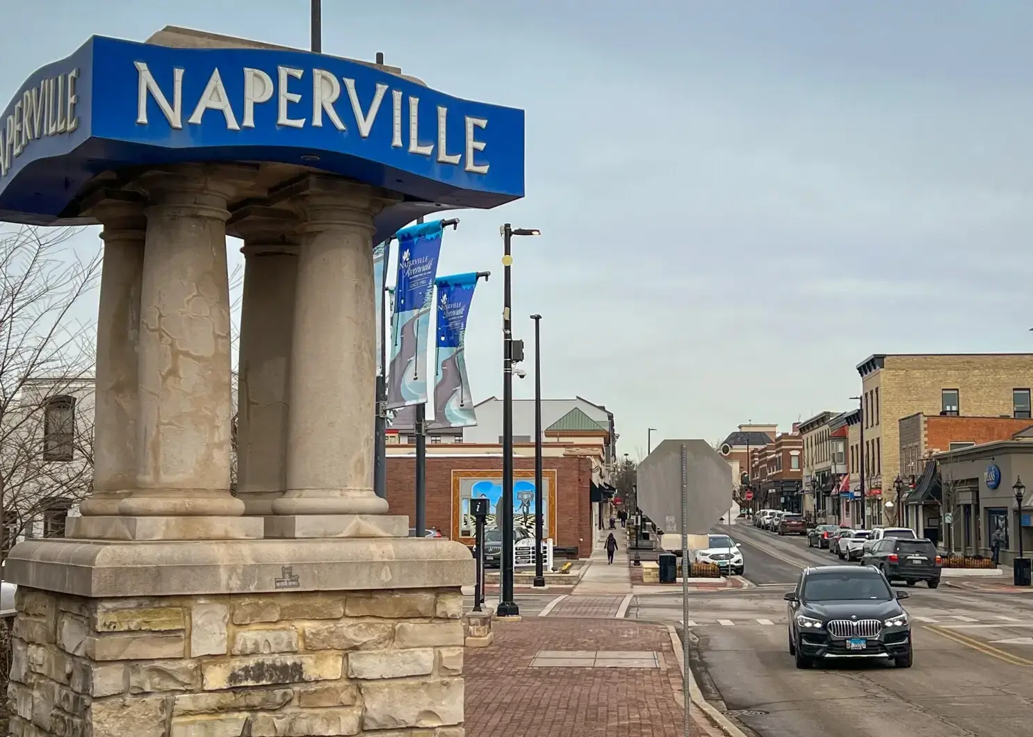 Blue Naperville, IL welcome sign showing a street in downtown Naperville with cars driving.